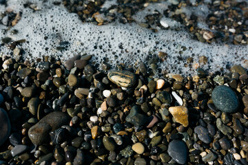 glossy stones washed by the sea wave shine from the rays of the sun on a summer day. pebbles on the city beach.the concept of environmental protection from pollution by petroleum products and plastics