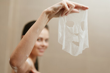 Young woman smiling while holding a facial mask in a spa-like environment, promoting self-care and beauty routines. Wellness and skincare concept.