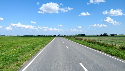 Fototapeta premium Scenic countryside road stretches into the distance under a beautiful blue sky with fluffy white clouds on a clear day