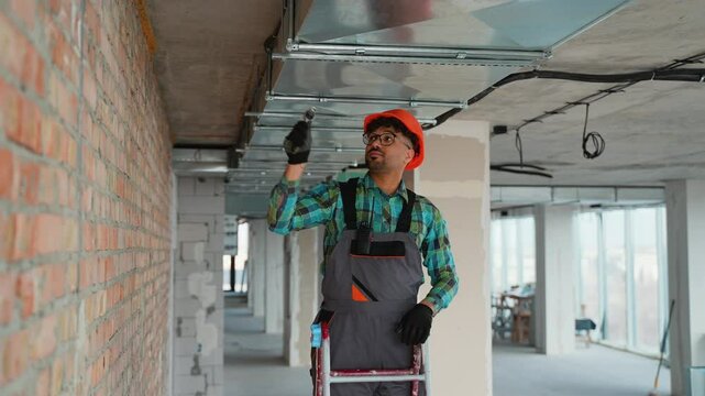 Electrician installing cable tray on ceiling in building under construction