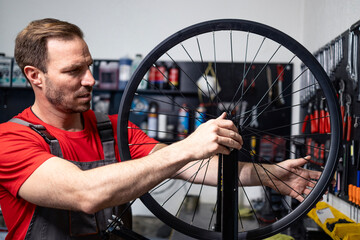 Professional serviceman repairing bicycle wheel in workshop.