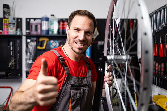 Portrait of experienced bicycle serviceman standing by bike wheel and holding thumbs up. - Powered by Adobe