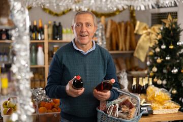 Elderly man buyer chooses bottle of whiskey in christmas decorated grocery store