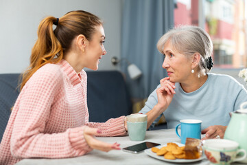 Senior woman talking with her granddaughter while they're drinking coffee in kitchen.