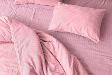 Cozy bed with soft pillow and crumpled pink duvet, top view