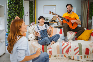 Caucasian man sit on sofa and play guitar for his female friends