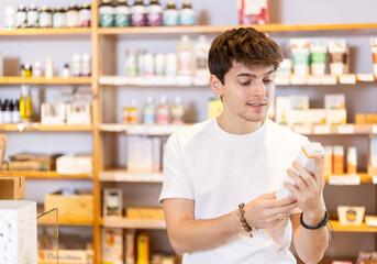In parapharmaceutical department, young man buy dietary supplement. Guy client selects vitamin and mineral complex to replenish deficiency of nutrients in body.