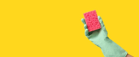 Hand in rubber glove holding sponge for cleaning on yellow background with space for text