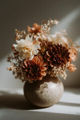 A bouquet of dried flowers in a textured ceramic vase. The arrangement features warm tones of brown, cream, and soft yellow, creating a cozy atmosphere.