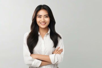 Studio portrait of a young asian businesswoman smiling with crossed arms, exuding confidence and professionalism against a gray backdrop