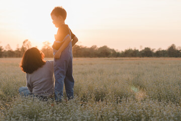 A mother and her young son are enjoying the golden hour in a peaceful meadow. Love, connection, family, childhood, peaceful, outdoor lifestyle, parenting, relaxation, seasonal campaigns. Mother's Day.