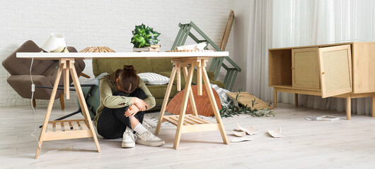 Young woman hiding under table in messy living room after earthquake