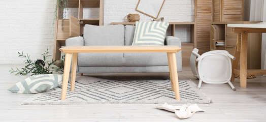 Interior of messy living room with sofa and tables after earthquake
