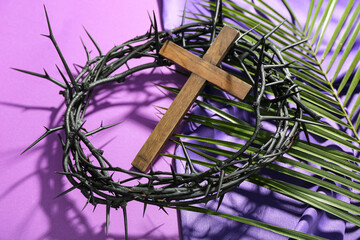Wooden cross with crown of thorns, palm leaf and purple fabric on violet background. Good Friday...