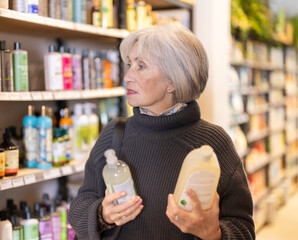 Customer takes out product options from shelf and selects shampoo or shower gel. Senior woman...