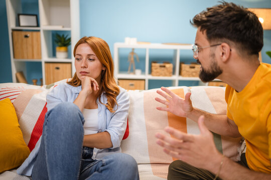 Caucasian stressed couple sitting on couch, arguing at home.