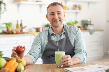 Mature man with glass of fresh smoothie and fruits in kitchen