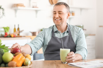 Mature man with glass of fresh smoothie and fruits in kitchen