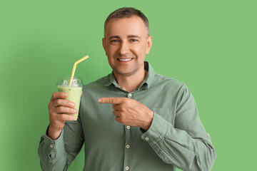 Mature man pointing at glass of vegetable smoothie on green background