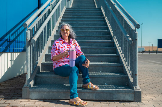 Stylish senior woman enjoying a refreshing drink on metal stairs