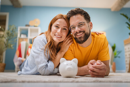 happy couple lying on floor and hold piggy bank, save coins together