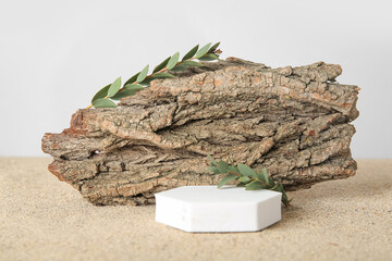 Decorative plaster podium with branches and tree bark on sand against white background