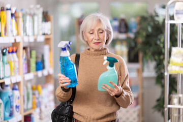 Elderly female shopper carefully selects a spray glass cleaner for windows in her home