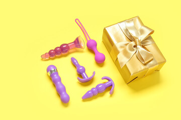 Composition with different sex toys and gift box on yellow background