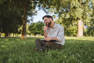 smiling businessman sit on grass in nature talk on mobile phone