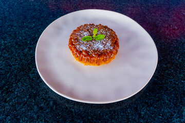 A delightful caramel cake topped with mint sits on a white plate, ready to enjoy.