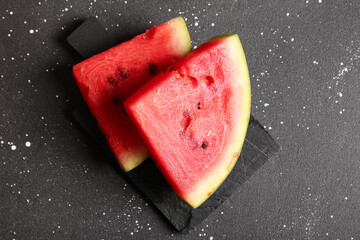 Board with pieces of fresh watermelon on black background