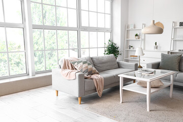 Interior of light living room with grey sofas and coffee table near big window