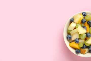 Bowl with fresh fruit salad on pink background