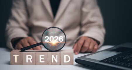 2026 trends concept. Businessman analyzing trends 2026 with magnifying glass and wooden cubes with...