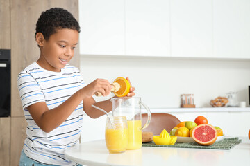 Little African-American boy making fresh citrus juice at table in kitchen
