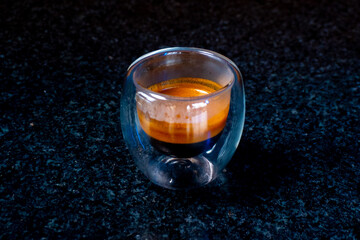 A close-up shot of a double-walled glass of espresso on a dark surface.