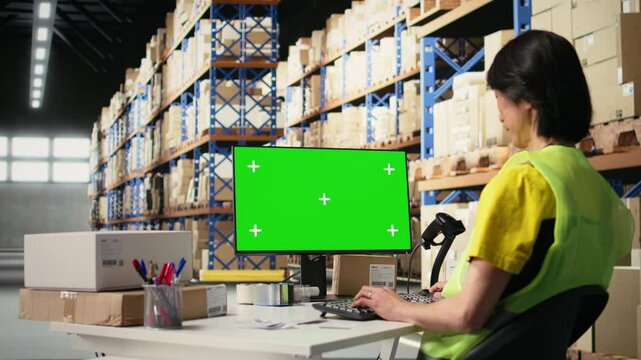 Staff reviews chroma key monitor in the stock room for data entry, inventory tracking mockups and visuals or barcode printer interfaces. Logistics worker packages cargo in the foreground. Camera A.