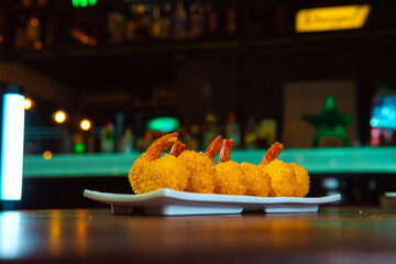 Crispy fried shrimp on a white plate, perfect for a delicious meal in a bar setting.