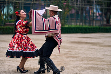 Portrait of a smiling young couple dressed as Chilean huasos, posing and joyfully dancing cueca...