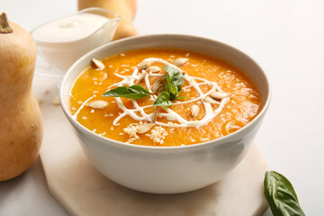 Bowl of delicious pumpkin cream soup with seeds and basil on white background