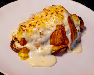 Close-up of a cheesy croissant sandwich with melted cheese and sauce on a white plate.