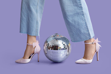 Female legs in stylish high heels with disco ball on purple background