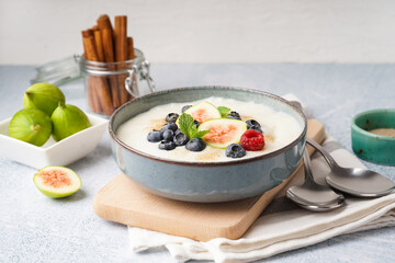 Bowl of tasty semolina porridge with fresh berries and figs on white background
