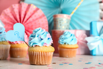 Delicious cupcakes with question mark, gift boxes and decorations on table against pink background....