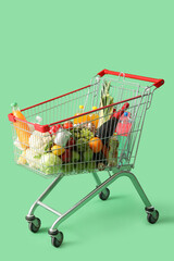 Shopping cart full of different food on green background