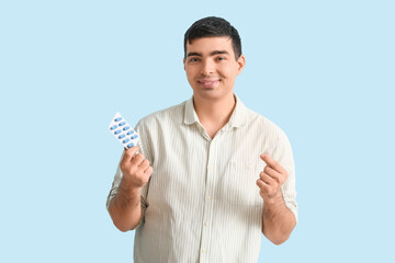 Young man with nasal drops and pills on blue background