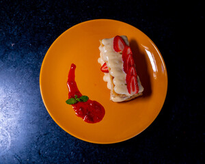 Elegant mille-feuille dessert with strawberries on an orange plate, ready to enjoy.