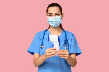 Portrait of female doctor in mask with infrared thermometer on pink background