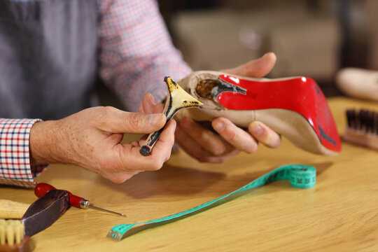 Mature shoemaker repairing broken heel at table in workshop, closeup