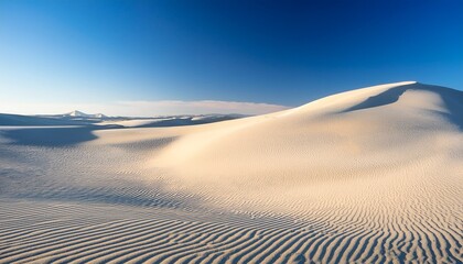white sand dunes under blue sky with long shadows and textured surfaces in a desert landscape